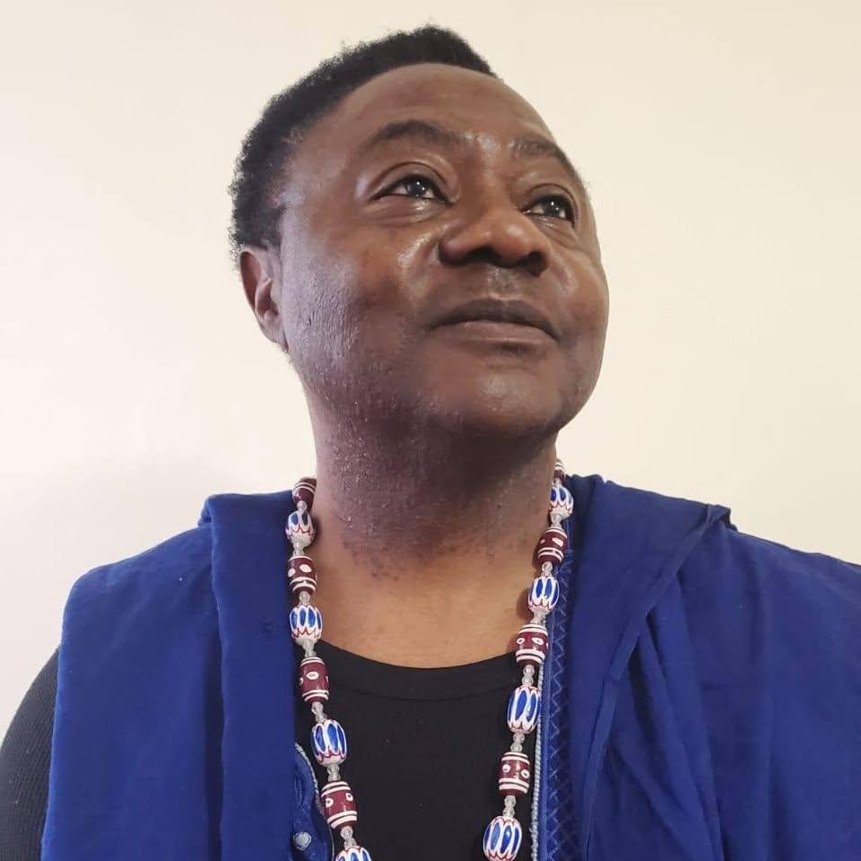 Portrait rapproché de JAH YAMS, veste bleue et collier de perles, regard tourné vers le haut