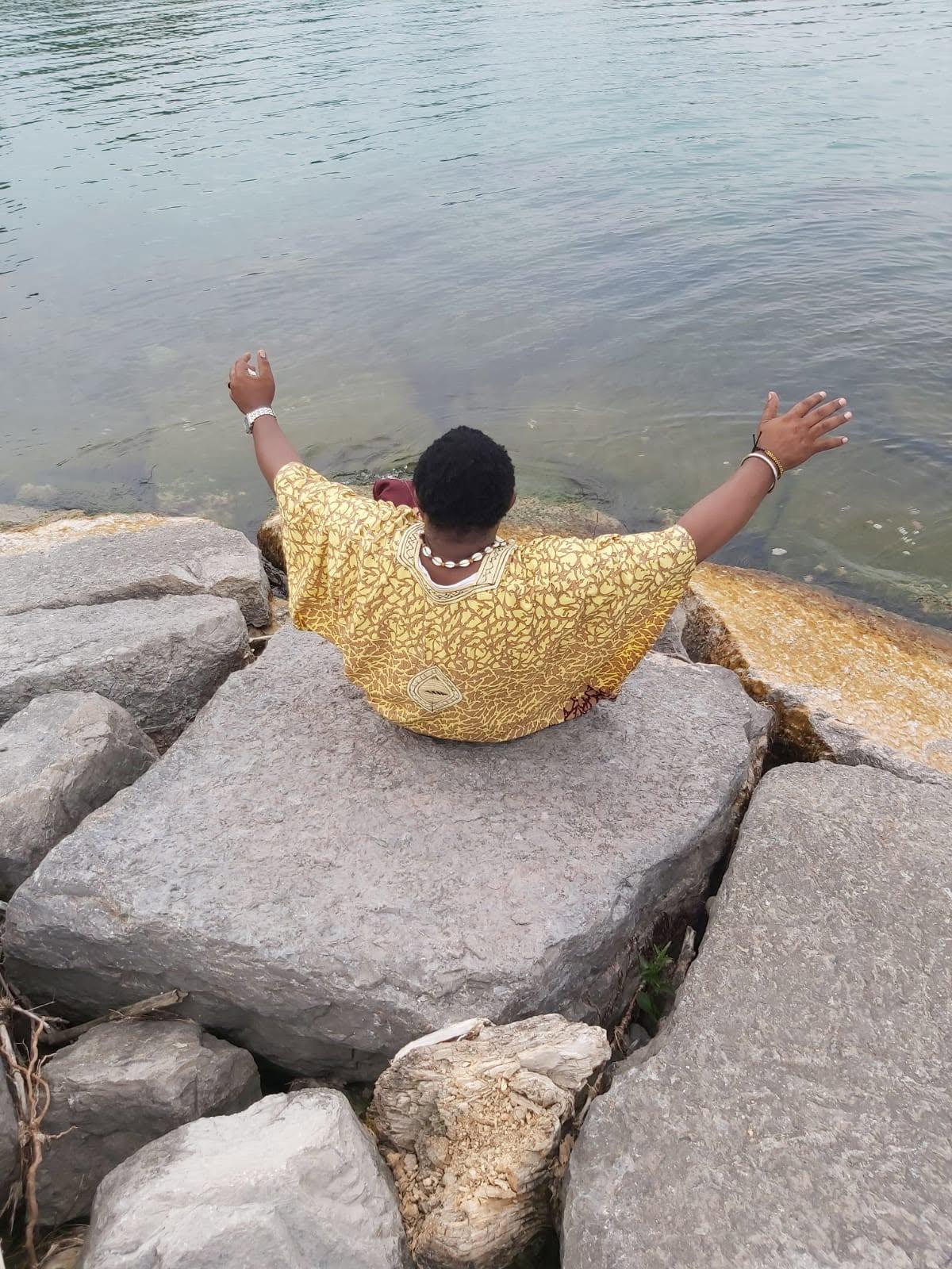 JAH YAMS de dos, bras ouverts face à l'eau, en tenue jaune